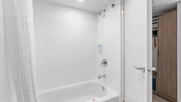 Un baño blanco con bañera, ducha y una puerta que da a un vestidor.