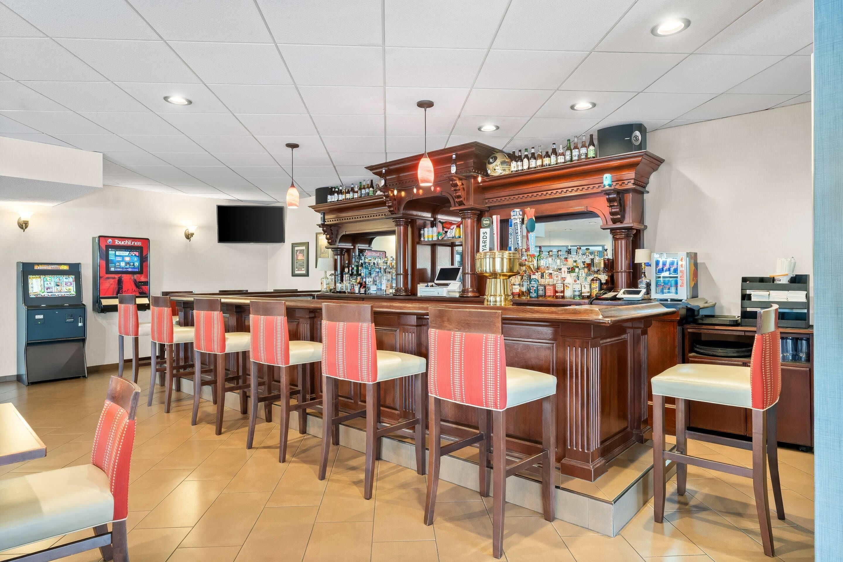 A bar area with wooden bar stools, a counter with a variety of bottles, and a television screen.
