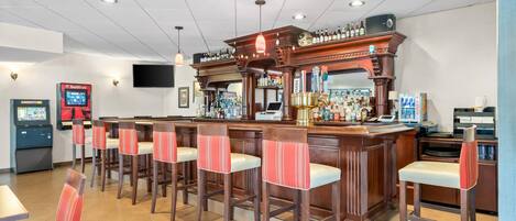 Zona de bar con taburetes de madera, una barra con una variedad de botellas y una pantalla de televisión.