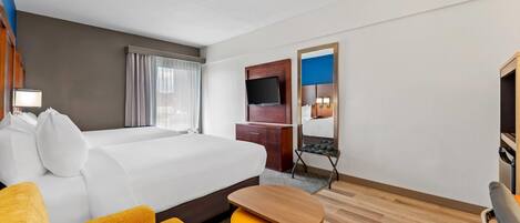 A hotel room with a bed, a desk, a television, a mirror, and a chair.