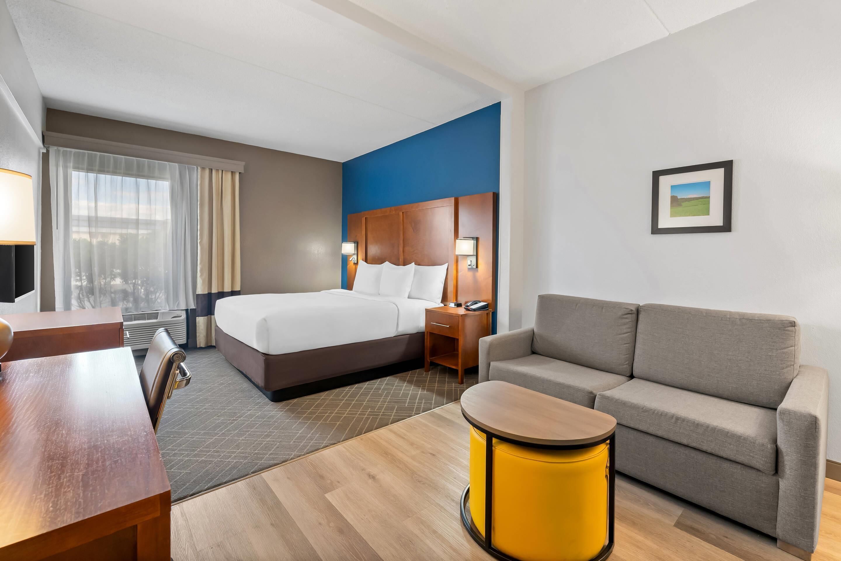 Une chambre d’hôtel avec un lit, un canapé, une petite table, une lampe et un tableau au mur.
