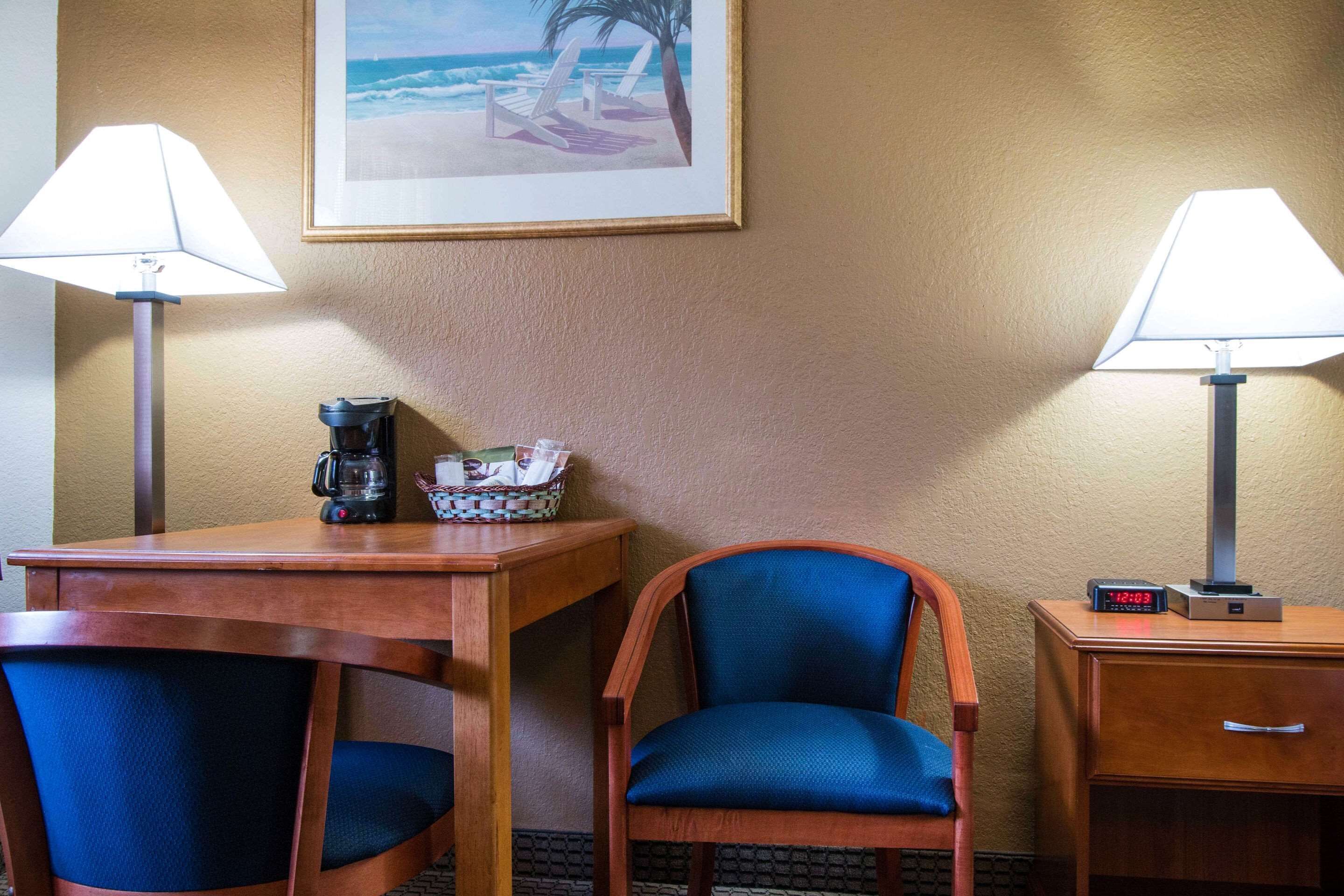 Ett hotellrum med ett träbord, två stolar, en lampa, en klocka och en inramad tavla på väggen.