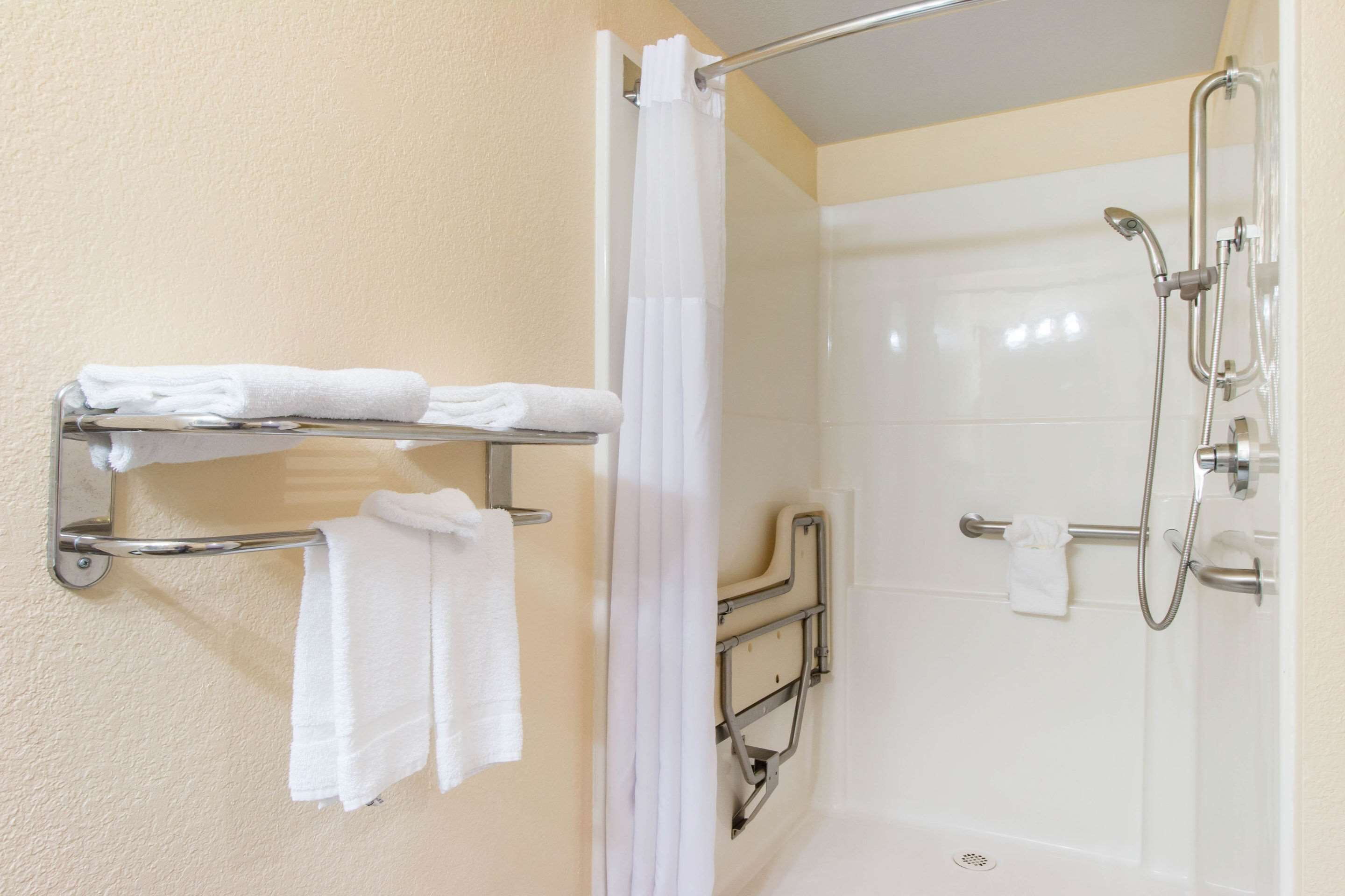 A bathroom with a shower, a towel rack with folded towels, and a grab bar.