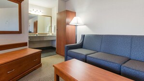 Une chambre d’hôtel avec une commode en bois, un canapé bleu, une table en bois et une lampe.