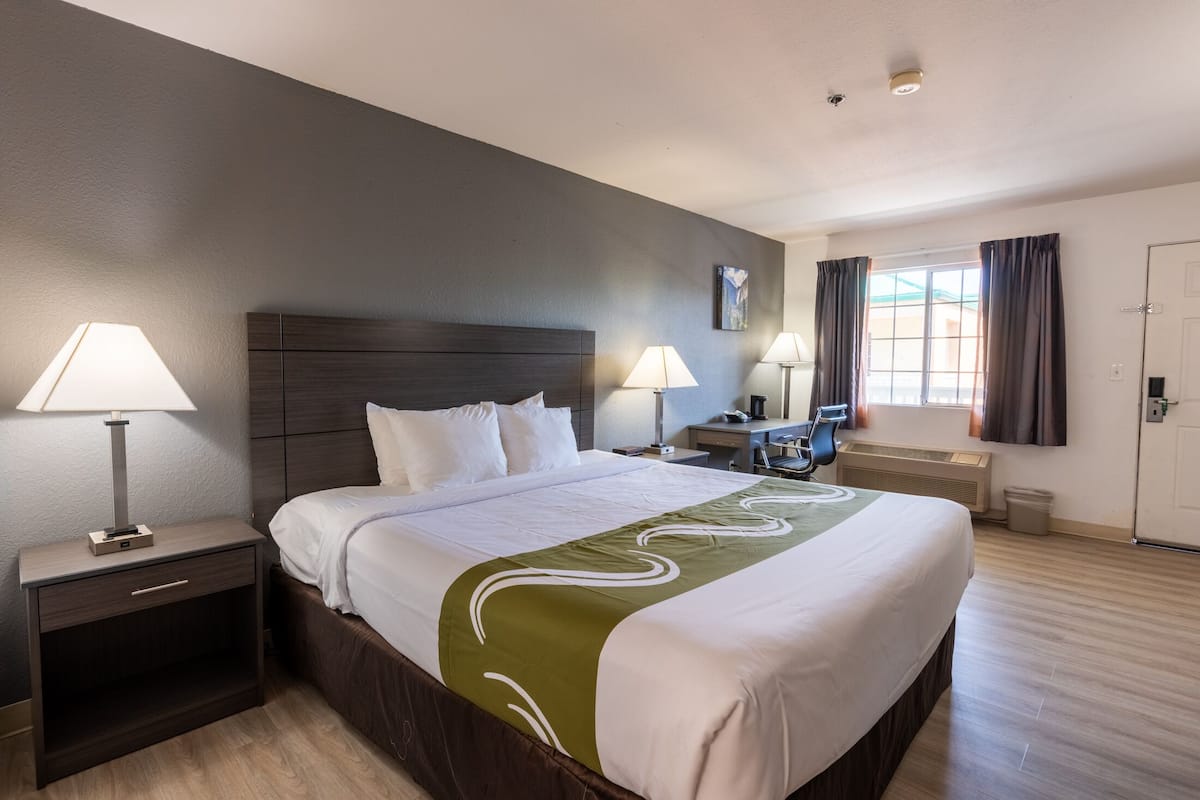 Hotelkamer met een groot bed, twee bedlampen, een nachtkastje, een bureau en een raam met gordijnen.