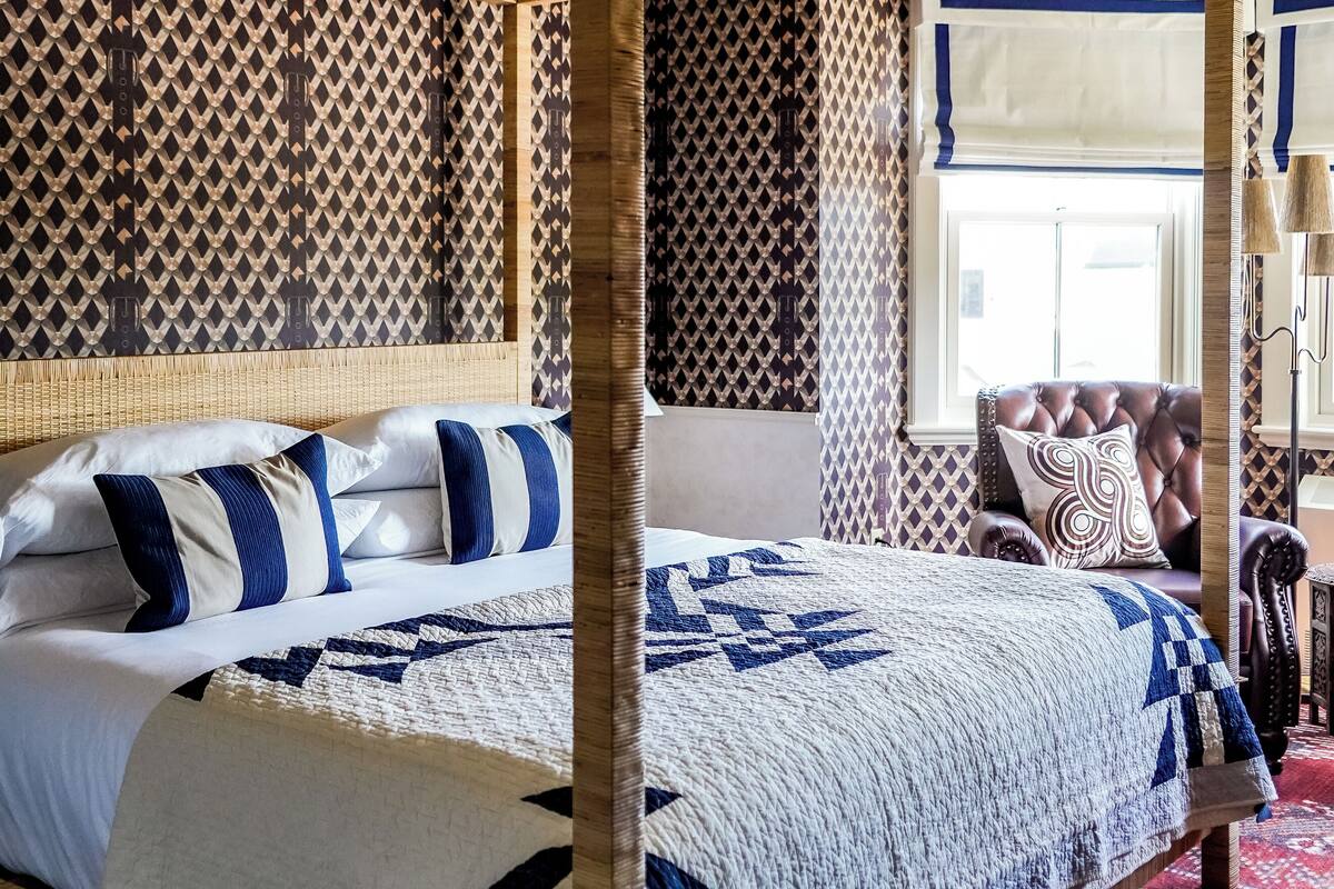 Una cama con dosel, un edredón estampado, un cabecero de madera y una alfombra roja con diseño.