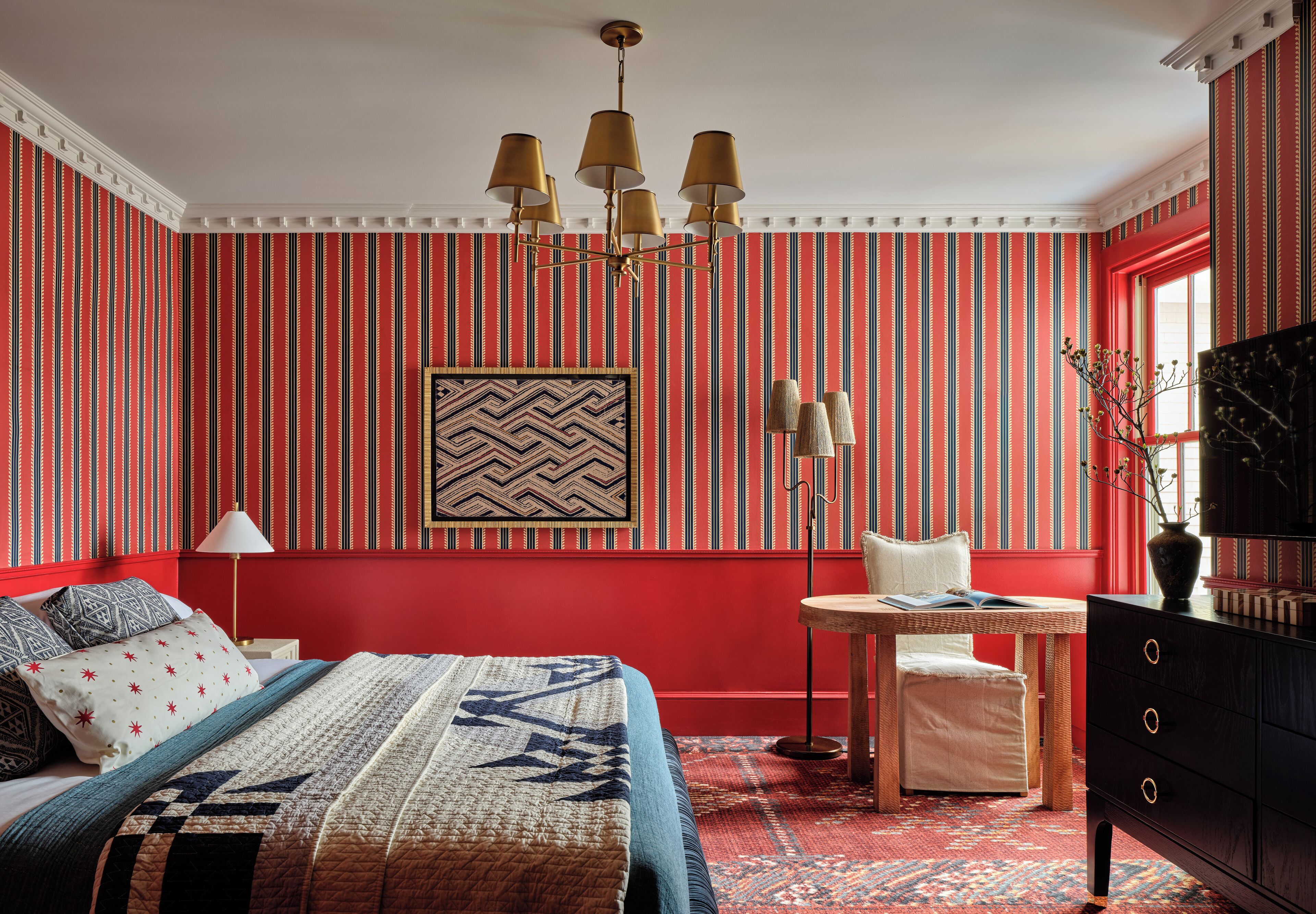 Ein Zimmer mit einem Bett, einem kleinen Tisch, einem Stuhl, einer Kommode und einer Wand mit vertikalen Streifen.
