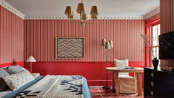 A room with a bed, a small table, a chair, a dresser, and a wall with vertical stripes.