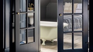 Puerta de madera oscura con un panel de vidrio que muestra un baño con bañera y ropa de cama a rayas.