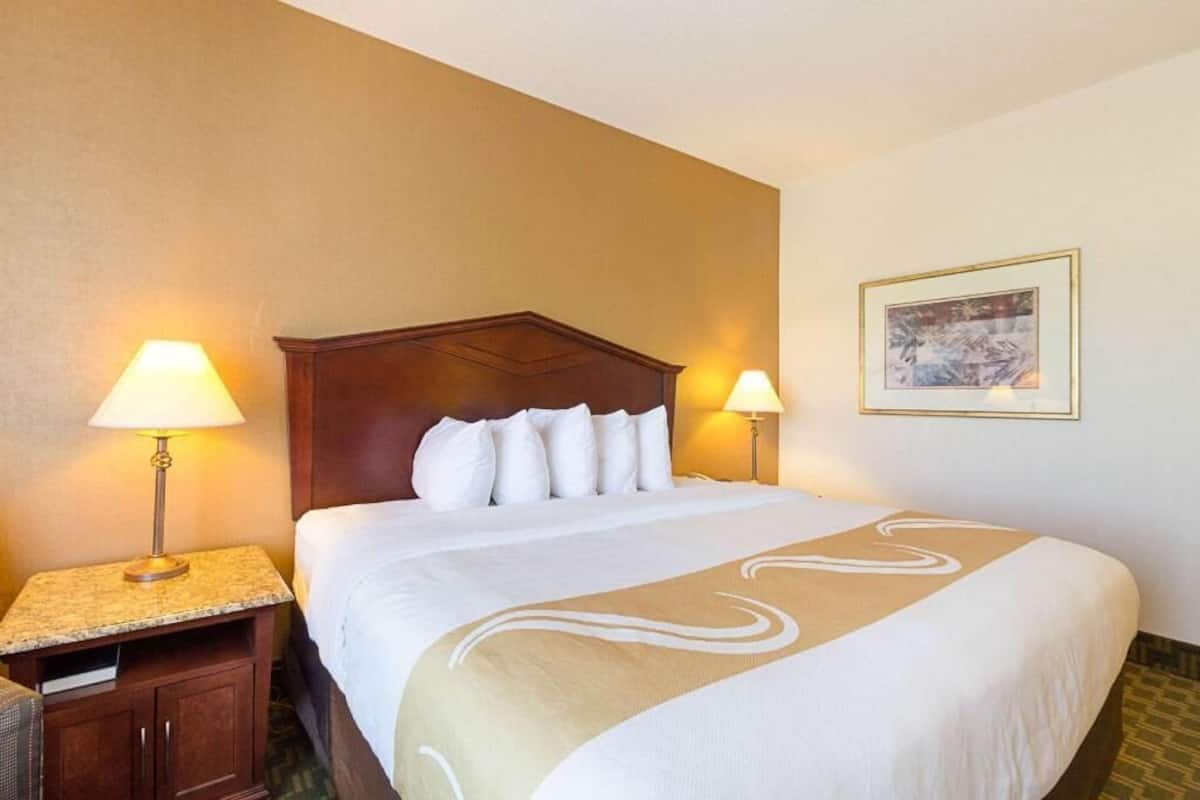 Una habitación de hotel con una cama grande, dos lámparas de noche, un cabecero, una mesita de noche, un escritorio y un cuadro en la pared.