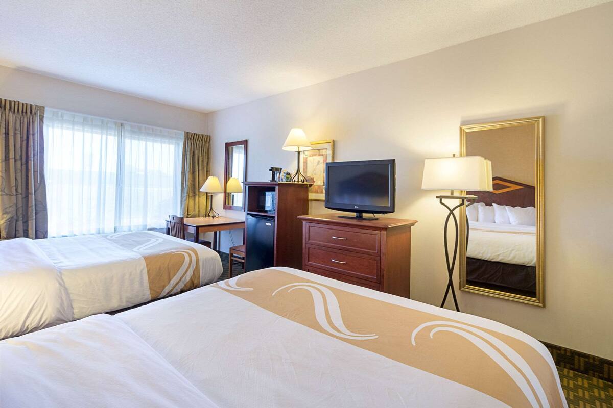Una habitación de hotel con dos camas, un escritorio, un televisor y un espejo.