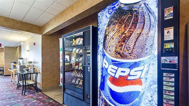 A vending machine with a Pepsi logo and a snack vending machine in a hotel lobby with a patterned carpet and a table with chairs.