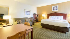A hotel room with a bed, two sofas, a dining table, and a TV.