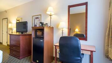 Et hotelværelse med skrivebord, stol, fjernsyn, minibar og to lamper.