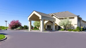 A hotel with a covered entrance, a parking lot, and a clear blue sky.