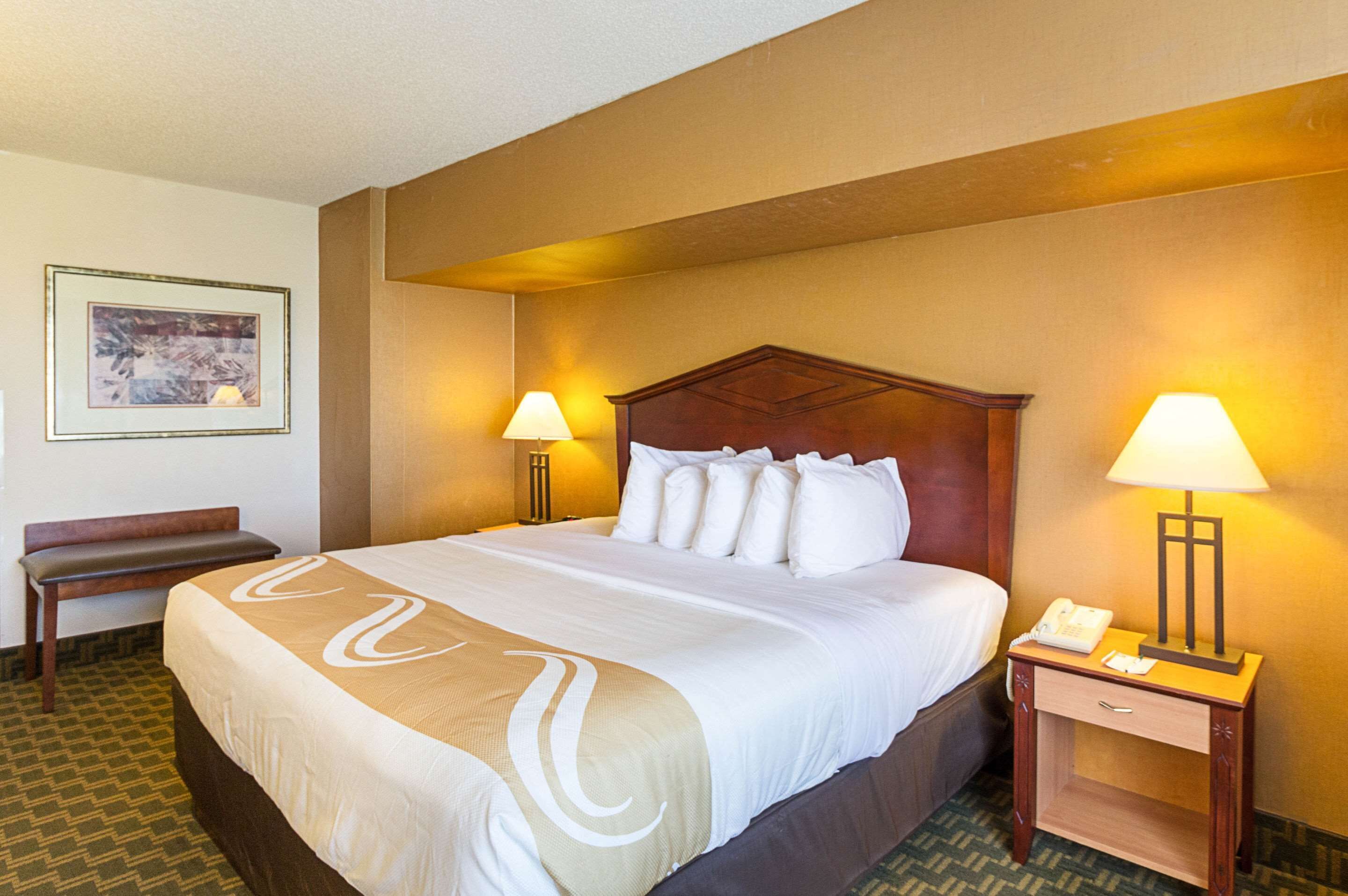Una camera d'hotel con un letto grande, due lampade sui comodini, un comodino con il telefono, una panca e un quadro appeso al muro.
