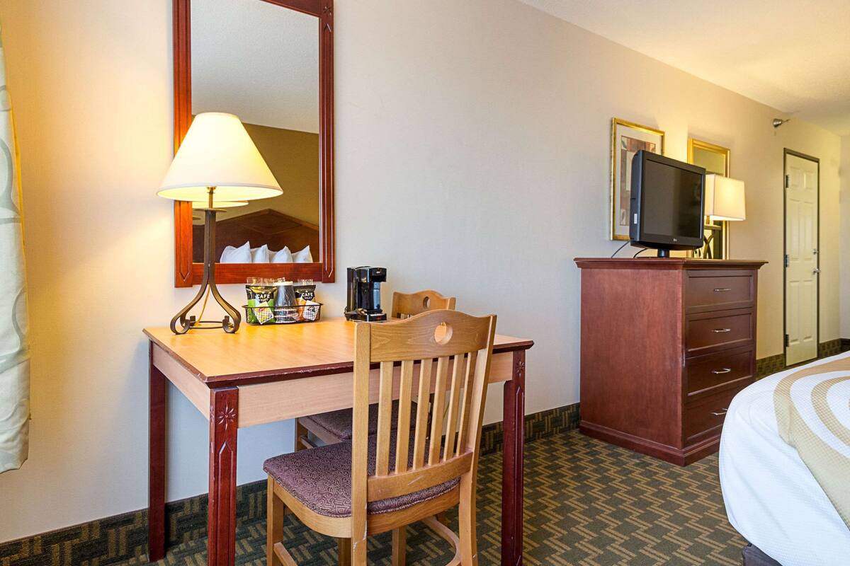 Una habitación de hotel con un escritorio de madera, una silla, un televisor sobre un mueble, un aparador y una cama.