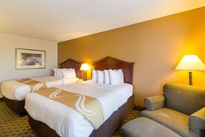 A hotel room with two beds, a sofa, and two lamps.