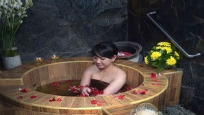 A woman in a wooden bathtub filled with water and rose petals, surrounded by statues and flowers. - The Jayakarta Jakarta (Jakarta)