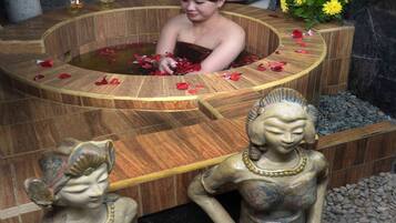 Relax in a serene spa setting with a central hot tub surrounded by a bench and candles, accompanied by statues of women.