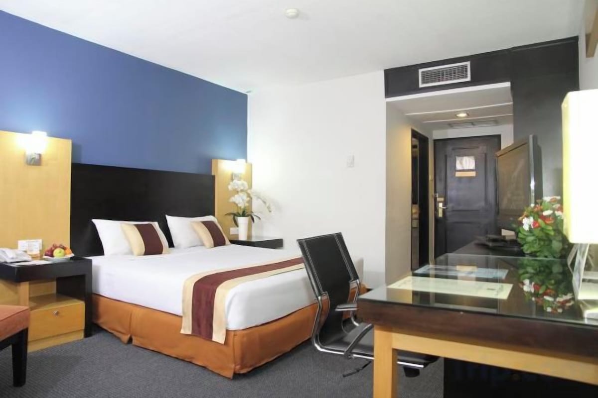A hotel room with a bed, bedside table, lamp, and a desk with a chair.