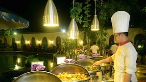 A buffet setup with various food dishes, a pool, and hanging lights. - The Jayakarta Jakarta (Jakarta)