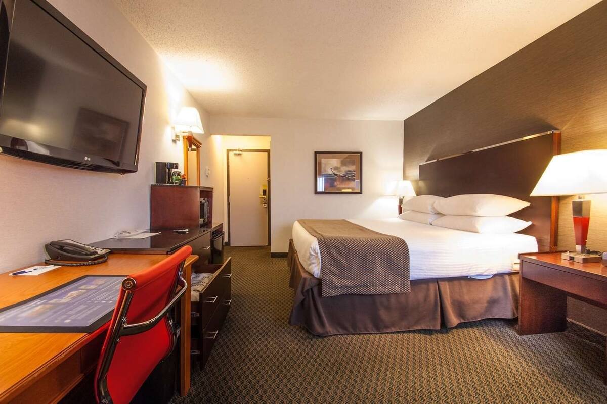 A hotel room with a bed, desk, chair, TV, and a painting on the wall.