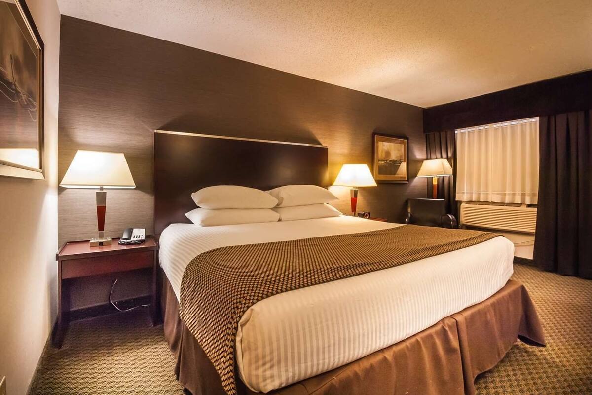 A hotel room with a large bed, two bedside tables with lamps, a window with curtains, and a painting on the wall.