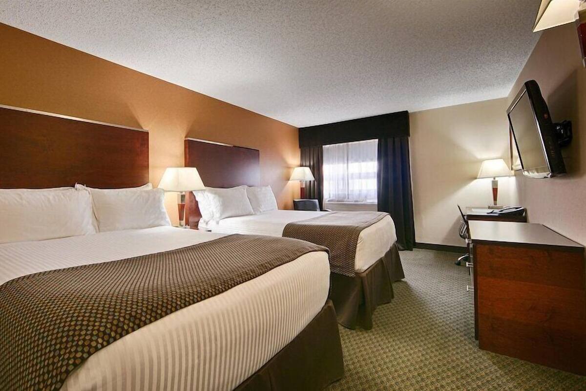 A hotel room with two beds, a desk, a chair, a TV, and a window with curtains.