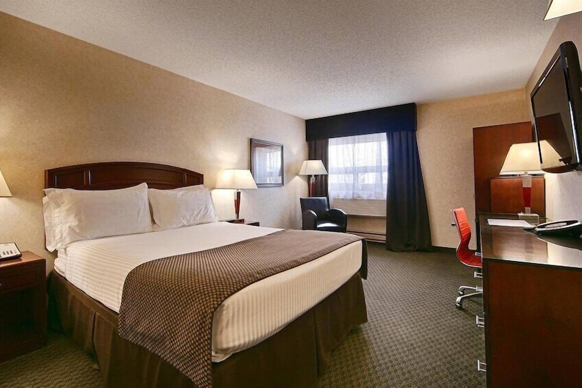 A hotel room with a large bed, bedside lamps, a desk with a chair, a TV, and a window with curtains.