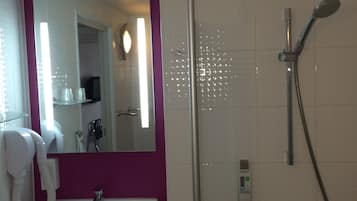 A bathroom with a white sink, a mirror, a shower with a handheld showerhead, and a handheld hairdryer.