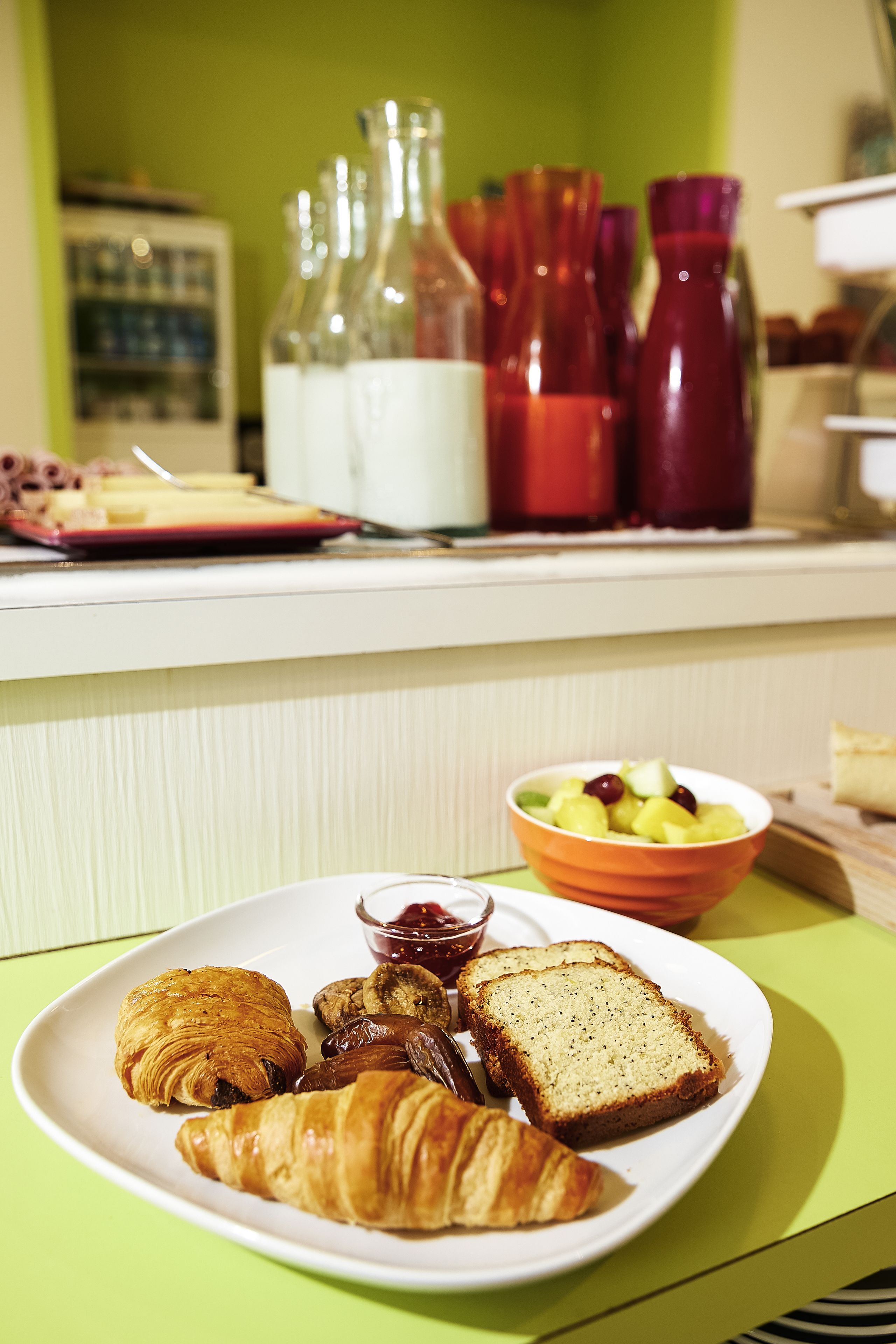 A breakfast plate with croissants, bread, and a fruit bowl on a table.