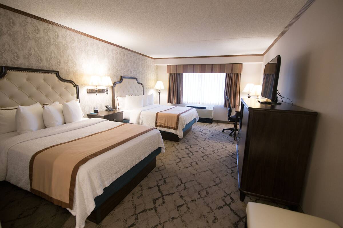 Una habitación de hotel con dos camas, un escritorio, una silla, un armario y un televisor.