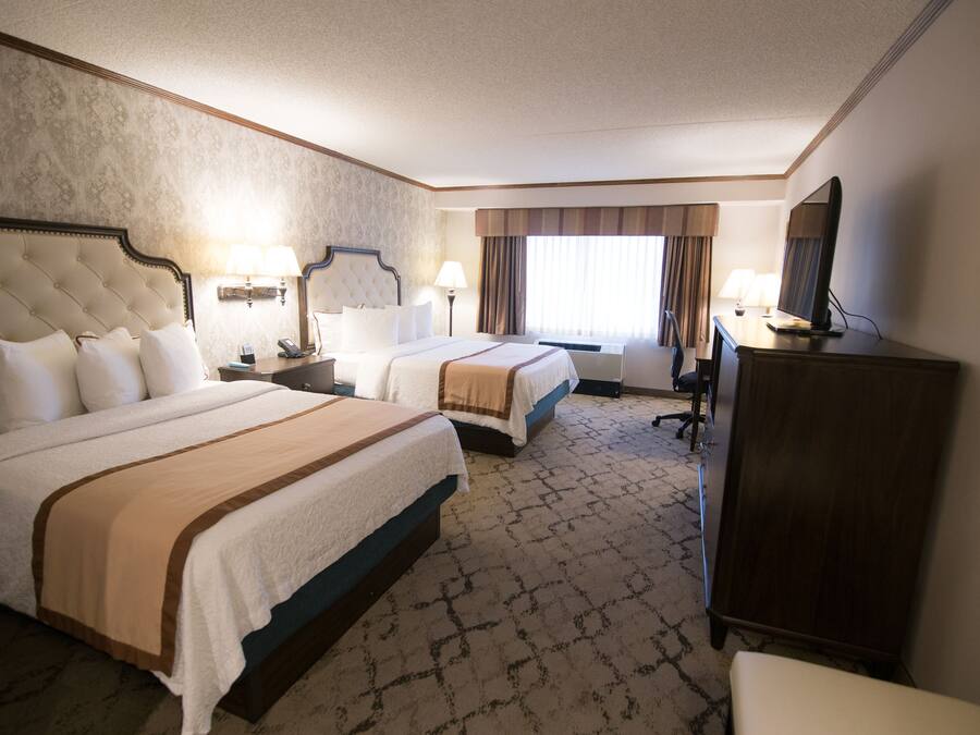 A hotel room with two beds, a desk, a chair, a wardrobe, and a television.
