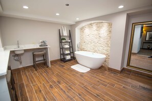 A modern bathroom with a freestanding bathtub, a wooden floor, a sink with a towel rack, and a shelf with towels. - Best Western Plus Fairfield Executive Inn (Fairfield)