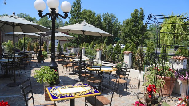 Un'area patio esterna con diversi tavoli e sedie, circondata da piante in vaso e ombrelloni.