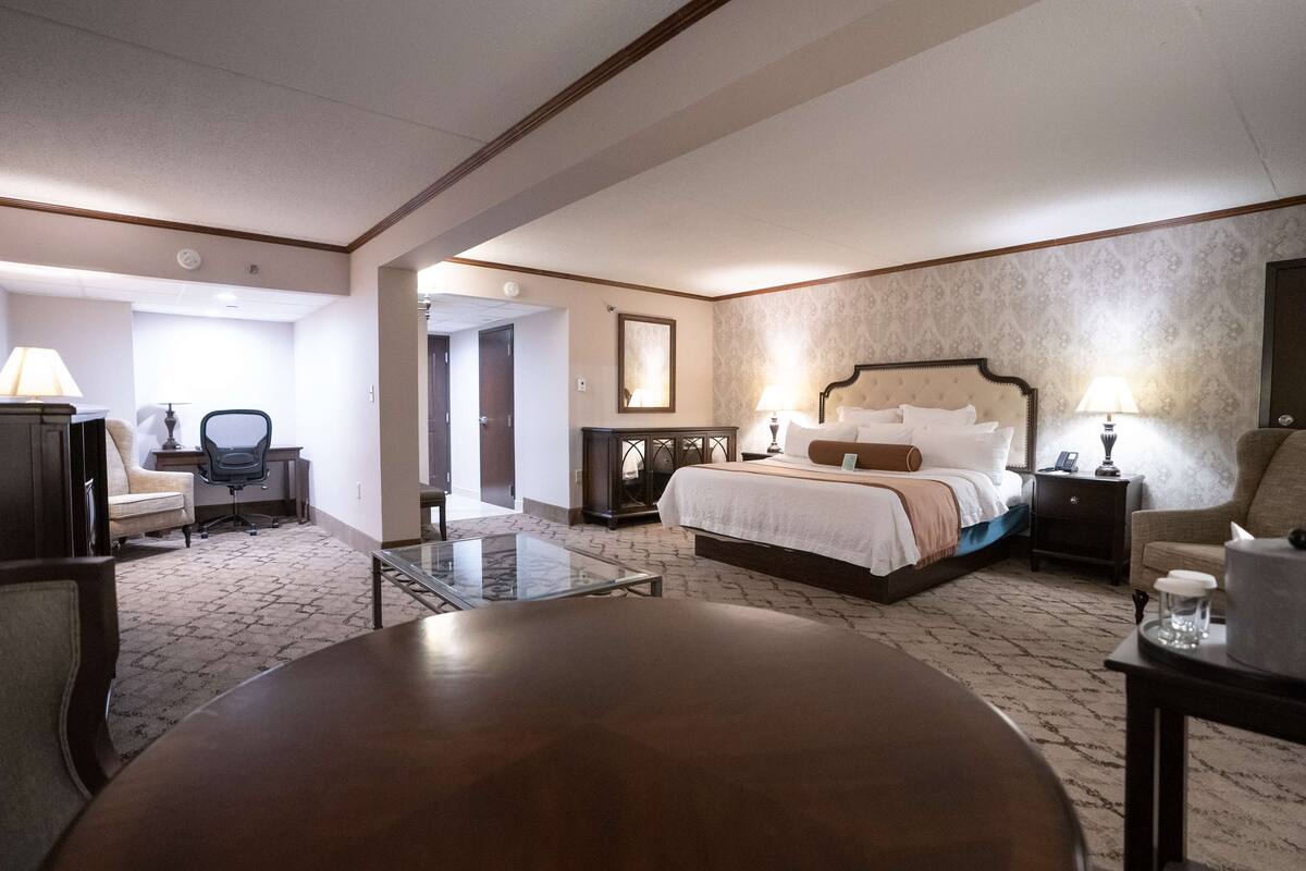 Una habitación de hotel con cama, mesitas de noche, un escritorio, una silla y una mesa de centro de vidrio.