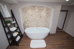 A modern bathroom with a freestanding bathtub, a wooden shelf with towels, and a tiled floor. - Best Western Plus Fairfield Executive Inn (Fairfield)