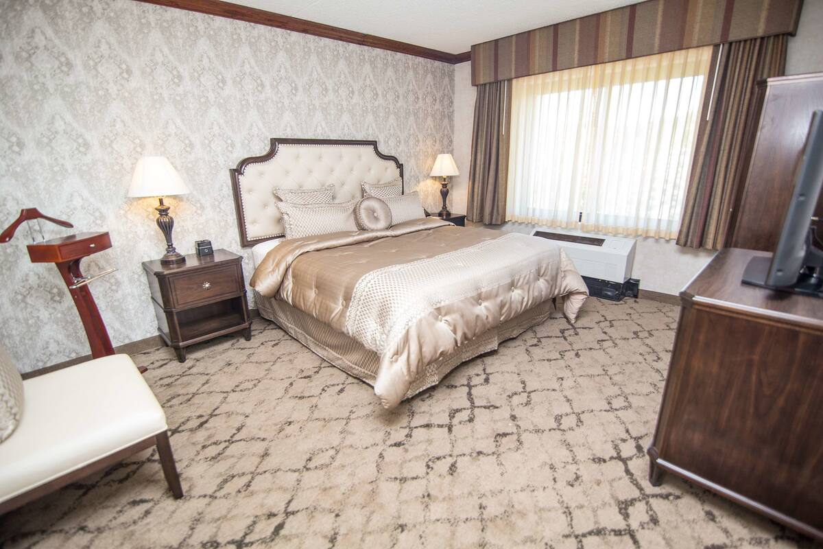 Una habitación de hotel con una cama grande, dos mesitas de noche con lámparas, un aparador de madera y un televisor.