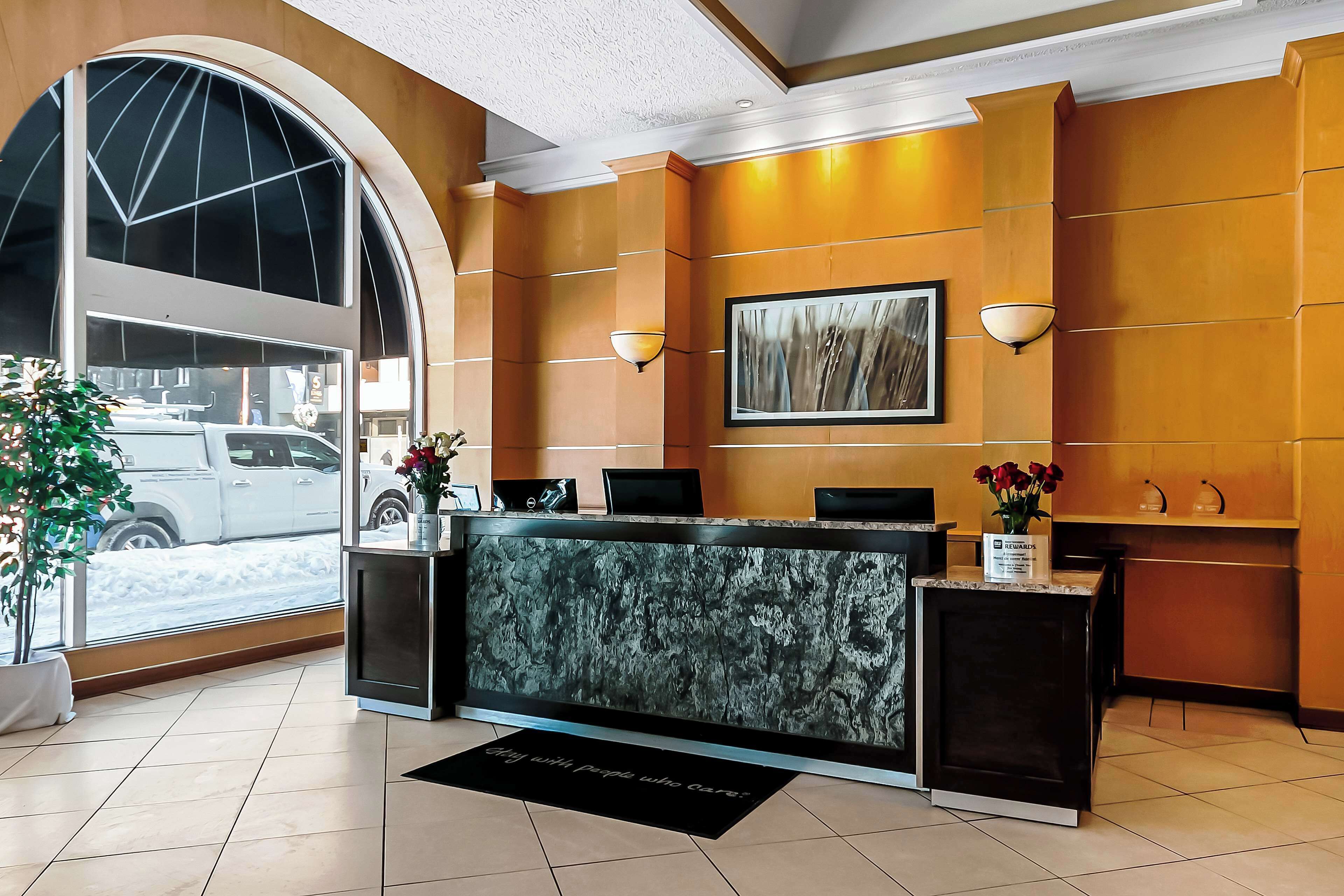 A hotel reception area with a marble reception desk, a large window with a view of a parked vehicle outside, and a framed artwork on the wall.