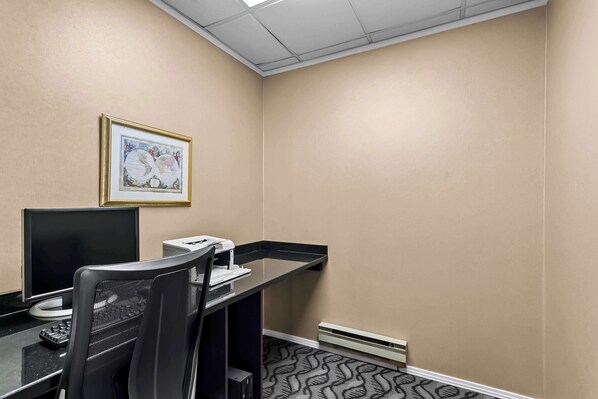 A hotel room with a desk, computer, and a framed picture on the wall.