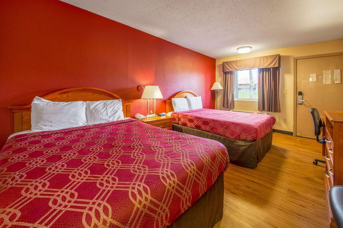 A hotel room with two beds, each with a red patterned bedspread, wooden headboards, and bedside lamps.