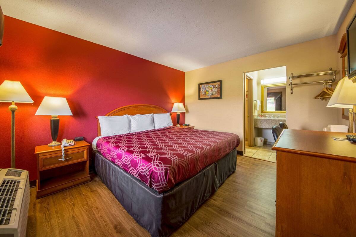 A hotel room with a large bed, two bedside tables with lamps, a wooden dresser, and a mirror.