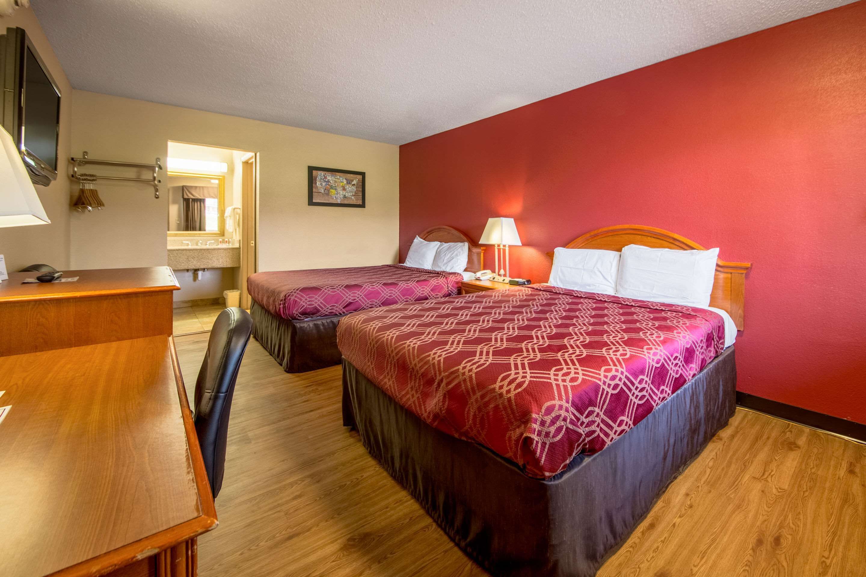 A hotel room with two beds, a desk, a chair, a TV, and a bathroom visible through an open door.