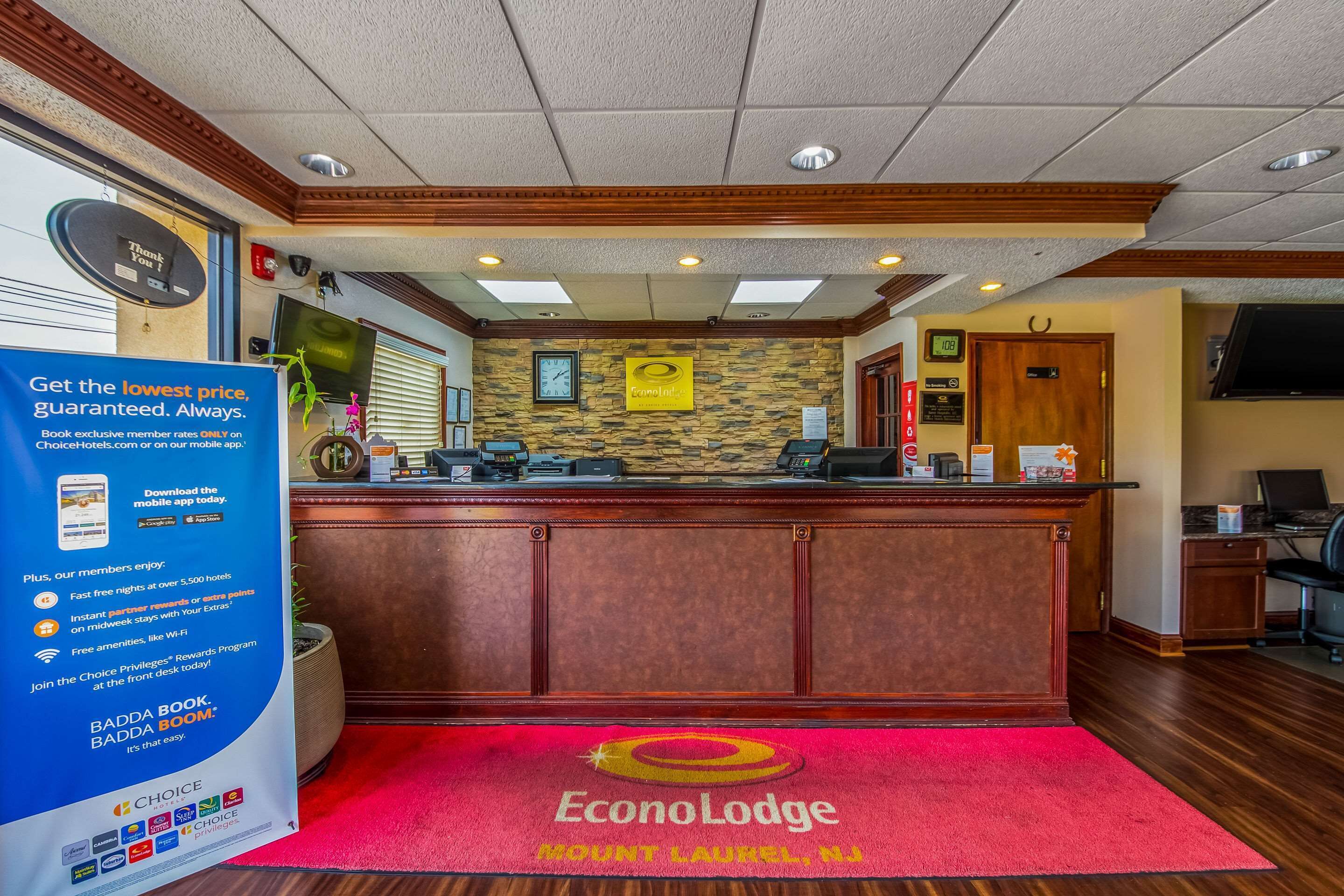 A reception area with a wooden desk, a red carpet with the EconoLodge logo, a clock, and a sign promoting the Badda Book program.