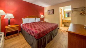 A hotel room with a large bed, two bedside tables with lamps, a wooden dresser, and a bathroom visible through an open door. - Econo Lodge Mount Laurel - Philadelphia East (Mount Laurel)