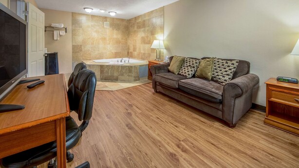 A modern room with a wooden floor, a sofa, a desk with a telephone, a TV, and a bathroom with a bathtub. - Econo Lodge Mount Laurel - Philadelphia East (Mount Laurel)