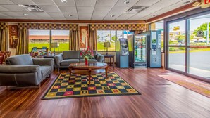 A lobby with a checkered carpet, leather sofas, a coffee table with flowers, an ATM, and a view of a green field and parking lot. - Econo Lodge Mount Laurel - Philadelphia East (Mount Laurel)