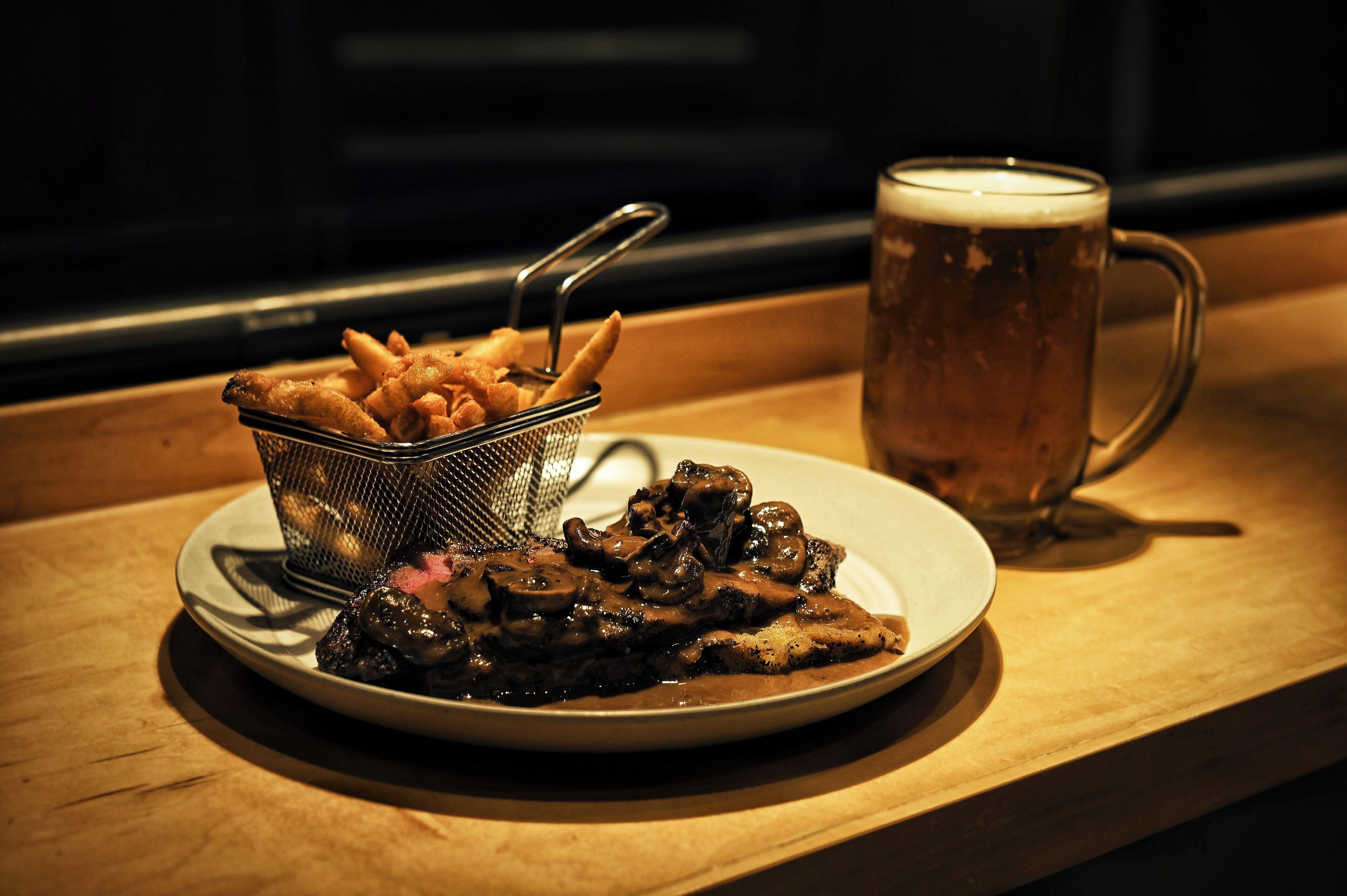 A plate of food with a side of fries and a glass of beer on a wooden table.