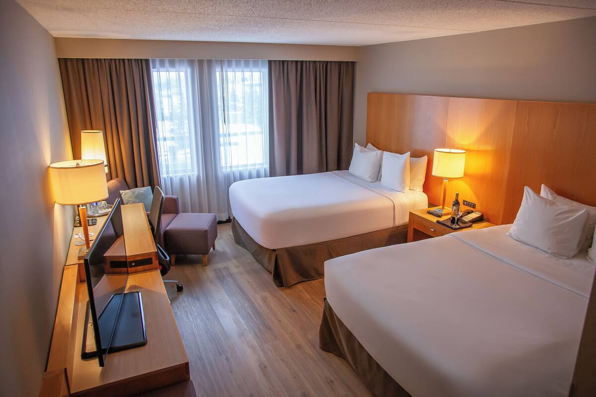 A hotel room with two beds, a desk with a computer, a chair, and a lamp.